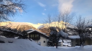 Ein verschneites Bergdorf mit traditionellen Holzhäusern, einem klaren Himmel und Blick auf die Berge im Hintergrund.