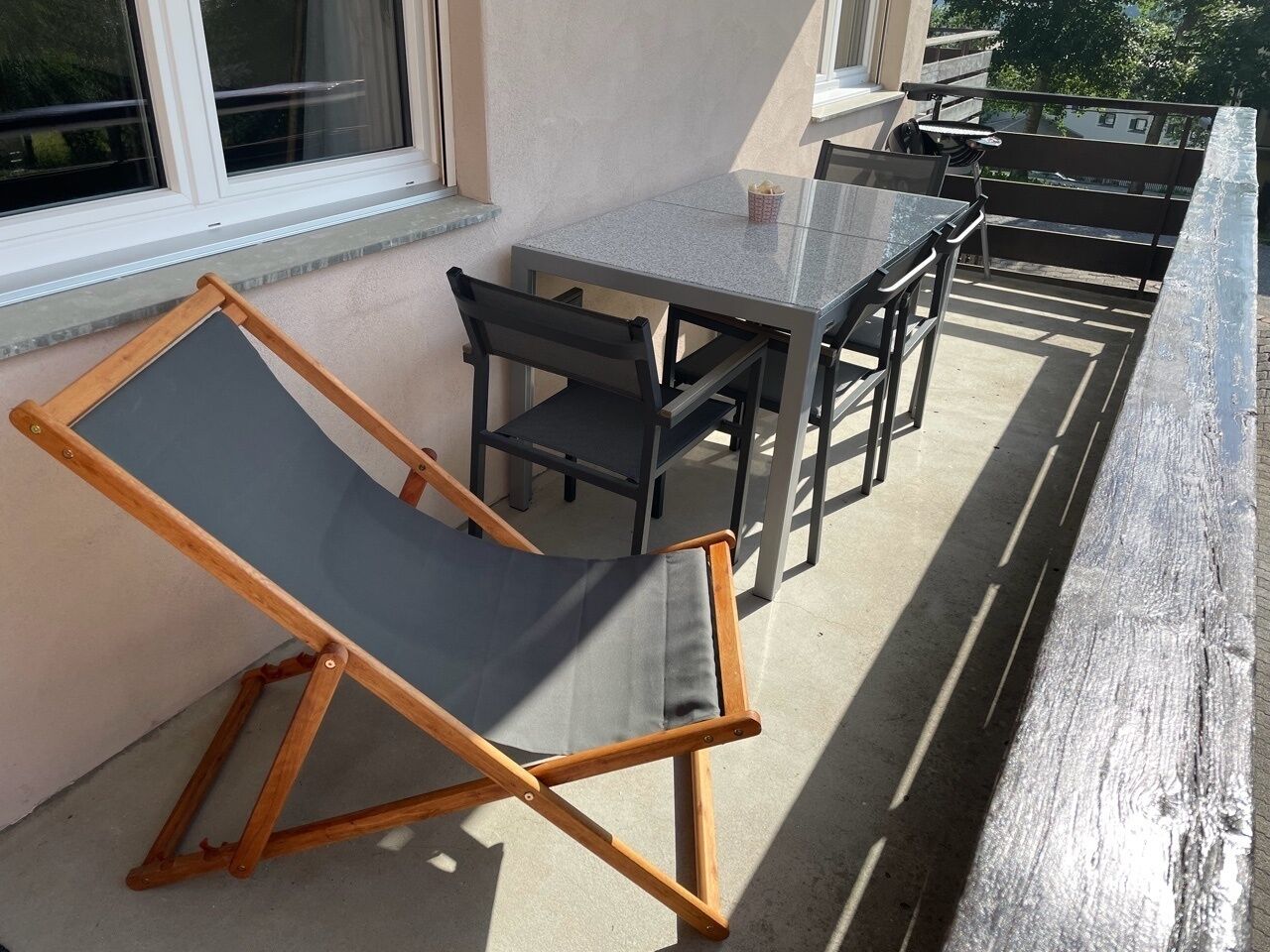 A balcony with a table and chairs, a wooden chair, and a window.