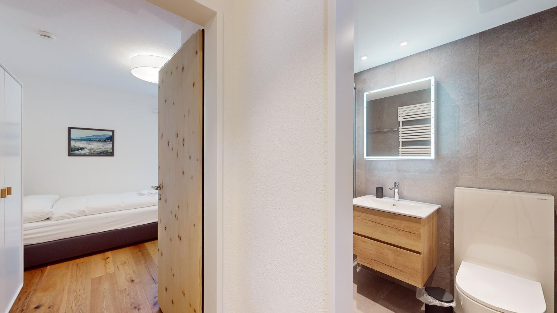 Une chambre à coucher moderne avec un lit, une porte en bois et une salle de bain équipée d’un lavabo, d’un miroir et de toilettes.