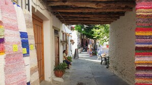 Eine schmale Gasse mit einer hölzernen Decke. Eine Frau sitzt auf einer Bank. An den Wänden hängen farbenfrohe Teppiche und in der Nähe der Bank steht ein Blumentopf.