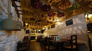 Um interior rústico com paredes de pedra, móveis de madeira e teto decorado com frutas penduradas.