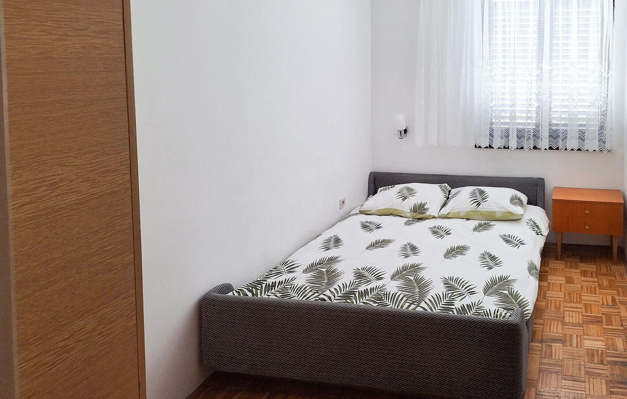 A small, neatly arranged bedroom with a bed, a nightstand, and a window with patterned curtains.