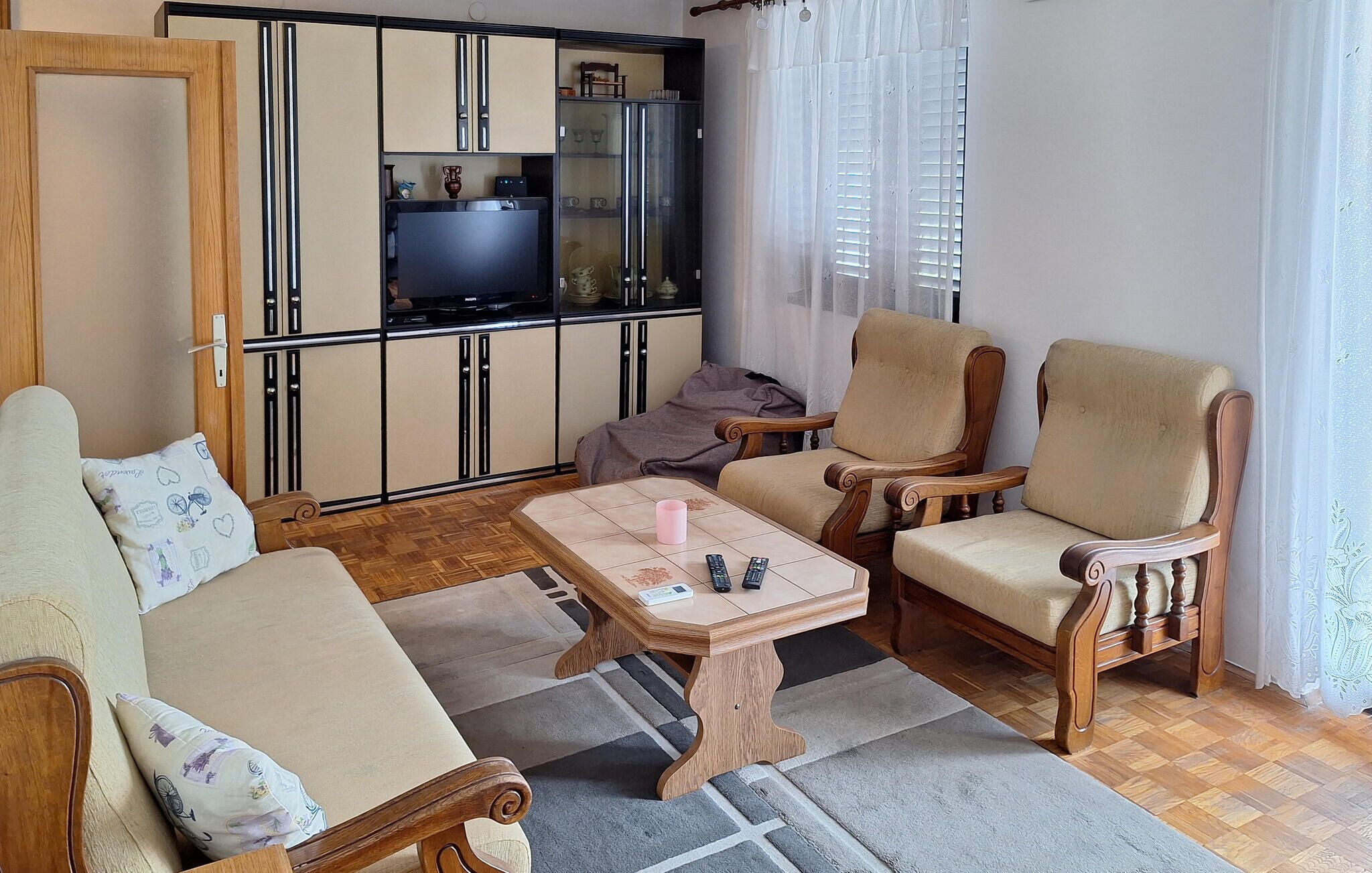 Un espace de vie compact comprenant un canapé, deux fauteuils, une table basse, un coin cuisine avec des placards et un réfrigérateur, ainsi qu’une fenêtre avec des rideaux.