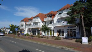 A row of white buildings with red roofs, balconies, and storefronts. - Vacation object Graal Müritz A1 - F01 (Graal-Müritz)