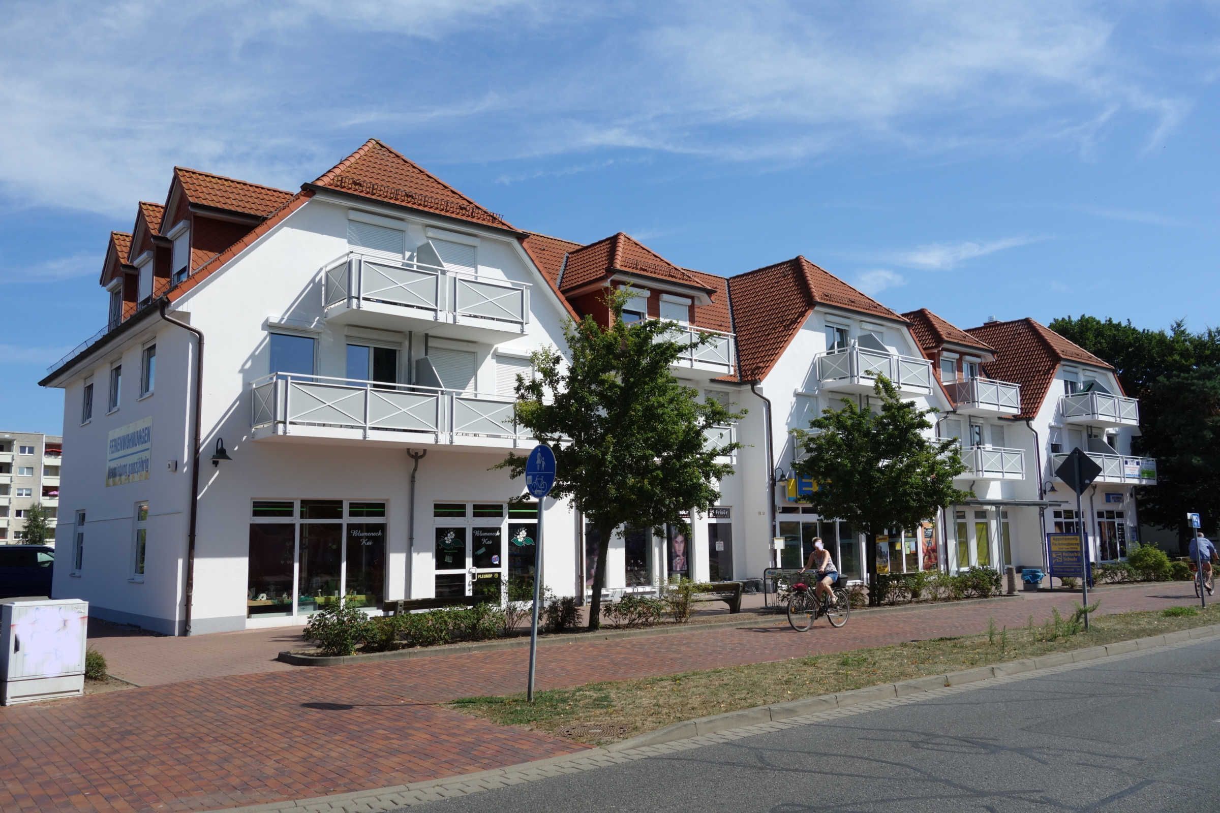 Eine Reihe weißer Gebäude mit roten Dächern und Balkonen, ein gepflasterter Weg und ein Radfahrer auf der Straße.