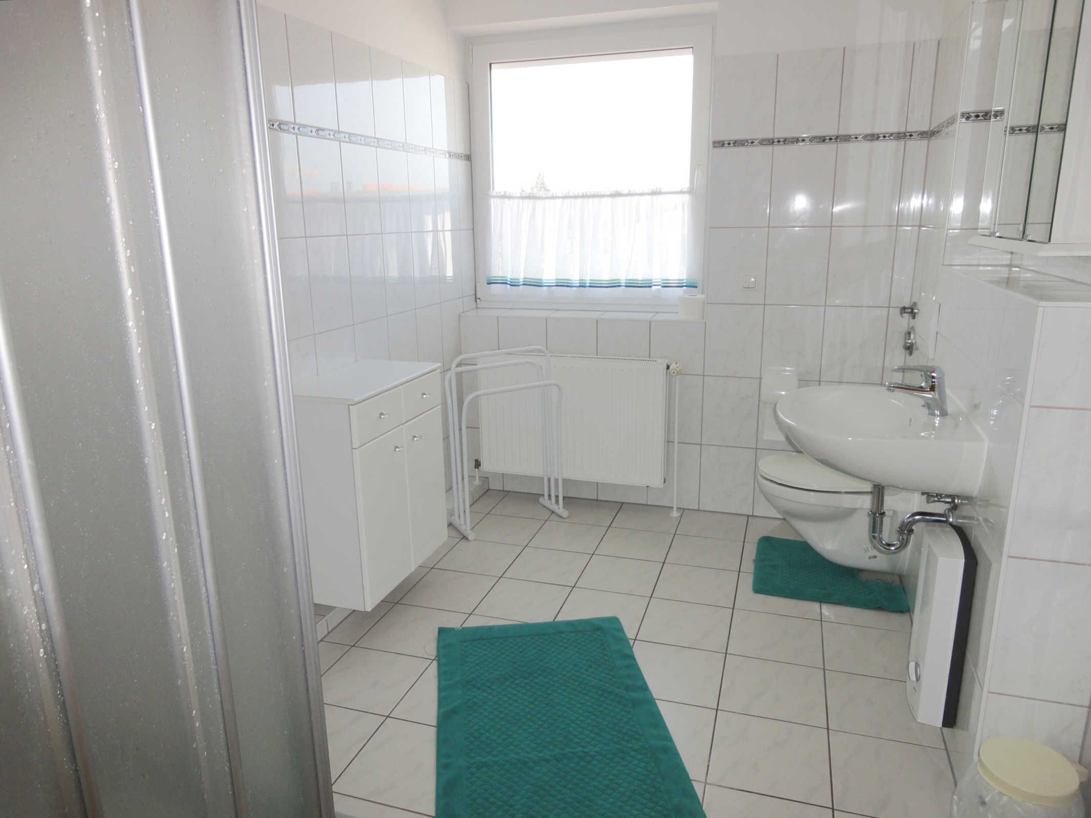 A bathroom with white tiles, a sink, a toilet, a window with curtains, and a radiator.