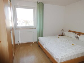 Een slaapkamer met een houten bed, een raam, een radiator en een groen gordijn.