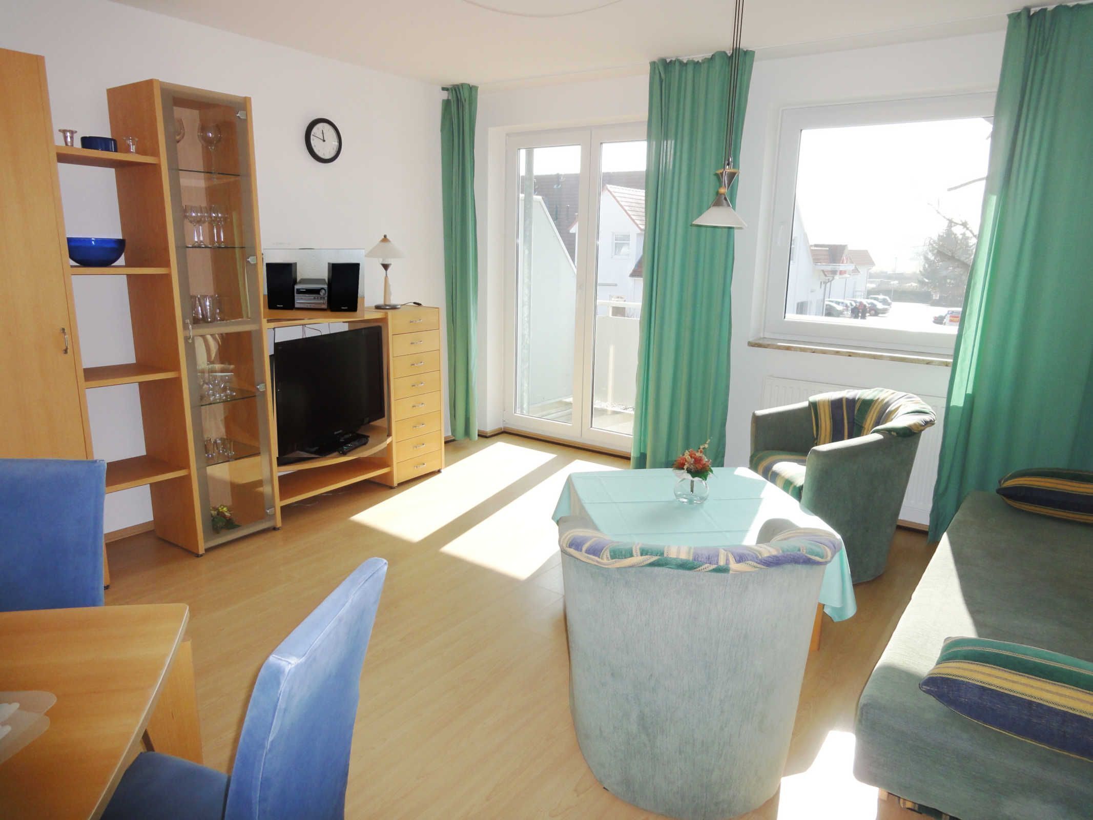 Een woonkamer met een televisie, houten planken, een eettafel en groene gordijnen.