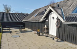 A building with a sloped roof, a wooden bench, a small table, and a wreath on the door.