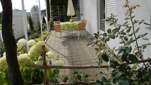 Un patio cubierto con una mesa y sillas, rodeado de plantas y una valla blanca.
