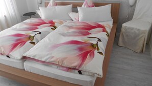 Una cama con colcha y almohadas estampadas con motivos florales, una mesita de noche y una silla.