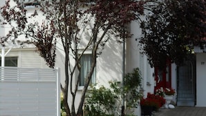 Un edificio residencial con entrada pavimentada, fachada blanca y puerta roja.