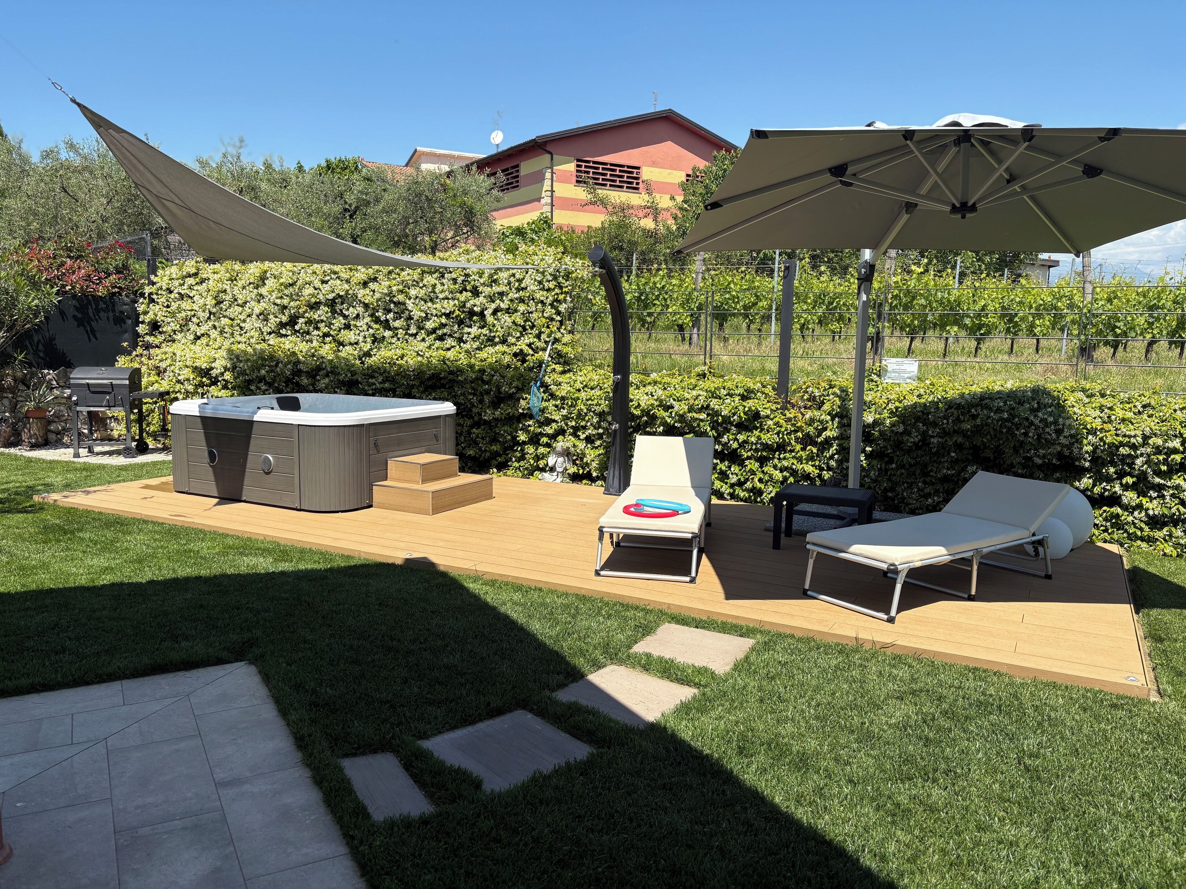 Ein Garten mit Whirlpool, Liegestühlen und einer Pergola, die Schatten spendet.