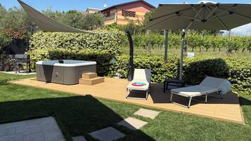 Ein Garten mit Whirlpool, Liegestühlen und einer Pergola, die Schatten spendet.