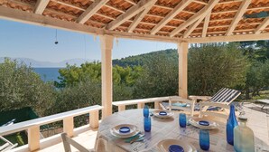 A covered outdoor dining area with a table set for two, overlooking a scenic landscape with trees and a body of water. - 2 bedroom gorgeous home in Postira (Postira)