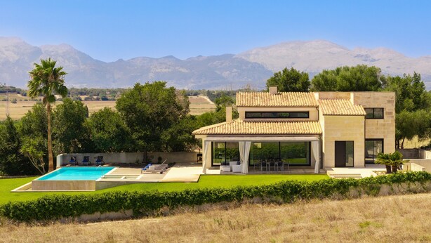 Una casa moderna de dos pisos con piscina, mobiliario exterior y vistas a las montañas.