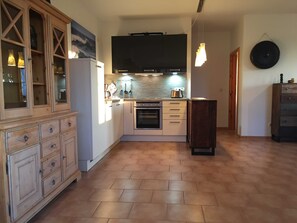 A compact kitchen with a built-in oven, a microwave, and a large black TV above the counter. There are wooden cabinets with glass doors and a small wooden cabinet to the right.