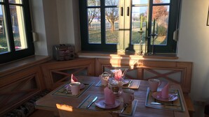A breakfast table set with pink cups, plates, and utensils, with a toaster and a coffee pot on the counter.