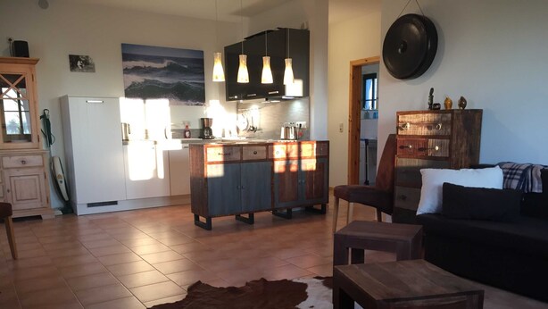A modern living room with a leather sofa, a coffee table, and a dining area with a kitchen in the background.