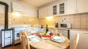 Une cuisine compacte équipée d’une cuisinière, d’un four à micro-ondes et de placards. On y trouve une table à manger avec des chaises, et une petite salade est posée sur la table.