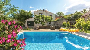 Une piscine à l’eau d’un bleu cristallin, entourée d’une végétation luxuriante et bordée d’un bâtiment doté d’un toit en pente.