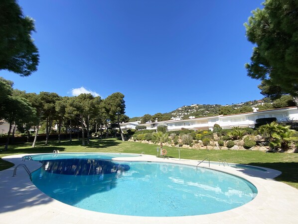 Une piscine à bord incurvé, entourée d’une pelouse bien entretenue et d’arbres.