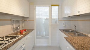 A compact kitchen with white cabinets, a gas stove, a sink, and a window with blinds. - Holiday rental apartment with swimming pool in Begur, Aiguablava (Begur)