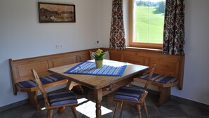 A dining area with a wooden table, bench seating, a vase with flowers, and a painting on the wall.