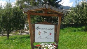 A wooden signpost with a sign that reads "Grossummerstall Gut Fam. Schwaab" surrounded by white flowers.