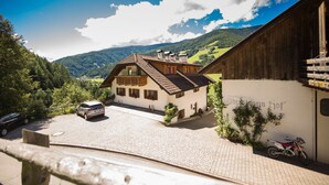 A traditional chalet with a sloped roof, a paved driveway, and a parked car. - Private apartment in the Dolomites: 2-8 persons (St. Lorenzen)
