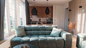 Ein modernes Wohnzimmer mit einer Eckcouch, einem Couchtisch und Blick auf eine Küche mit Holzausstattung und einer Mikrowelle.