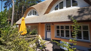 Une maison avec un toit de chaume, de grandes fenêtres et un parapluie jaune.