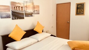 A bedroom with a bed, two pillows, a wooden door, and three wall-mounted pictures. - White Villa Airport Transit Hotel (Seeduwa - Katunayake)