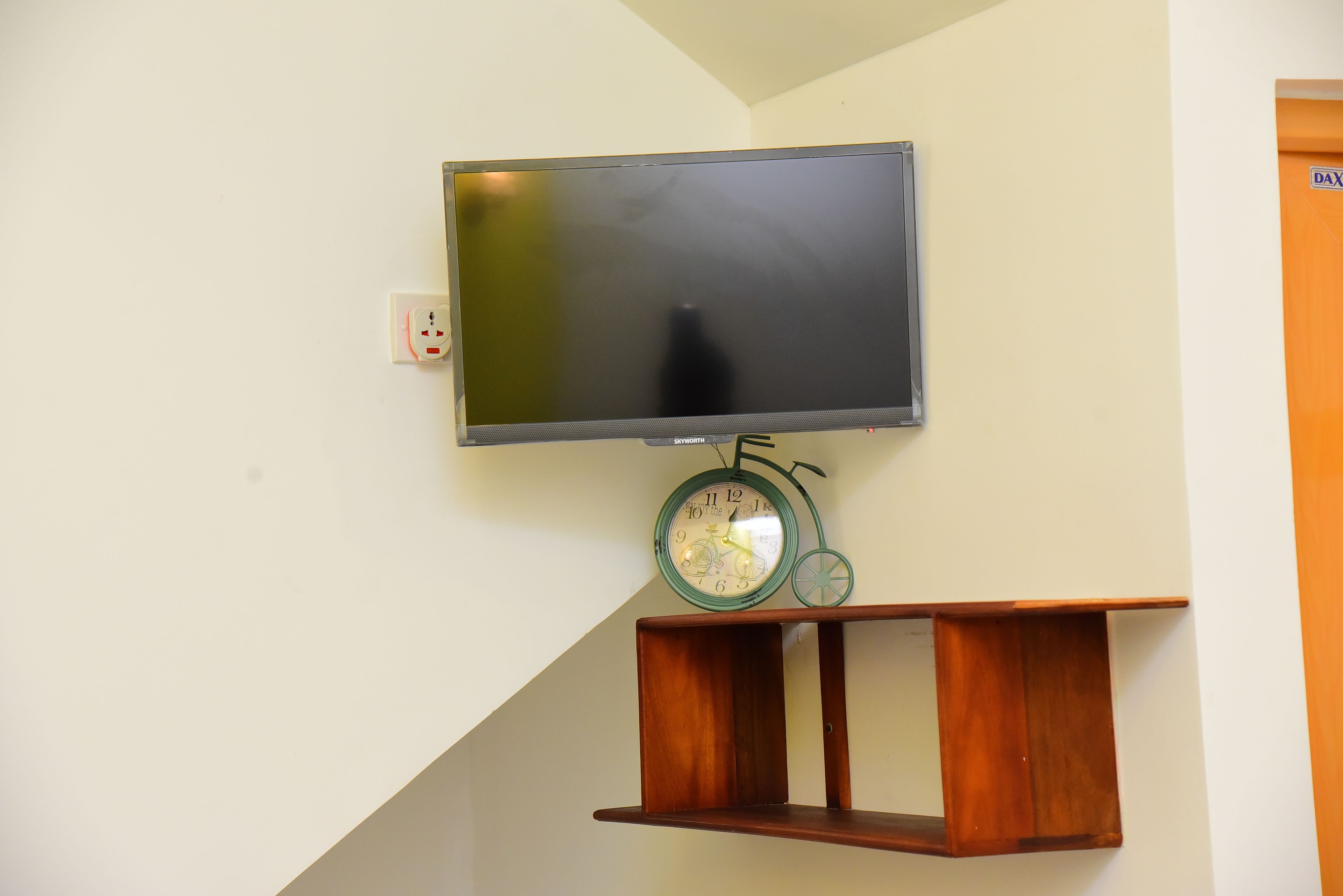 A flat-screen TV mounted on a wall above a wooden shelf.