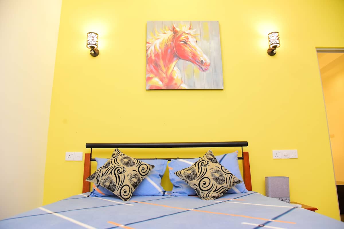 A bed with a blue and white striped bedspread, two patterned pillows, and a painting of a horse on the yellow wall above.