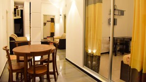 A modern living room with a wooden dining table and chairs, a sofa, and a glass partition with curtains. - White Villa Airport Transit Hotel (Seeduwa - Katunayake)
