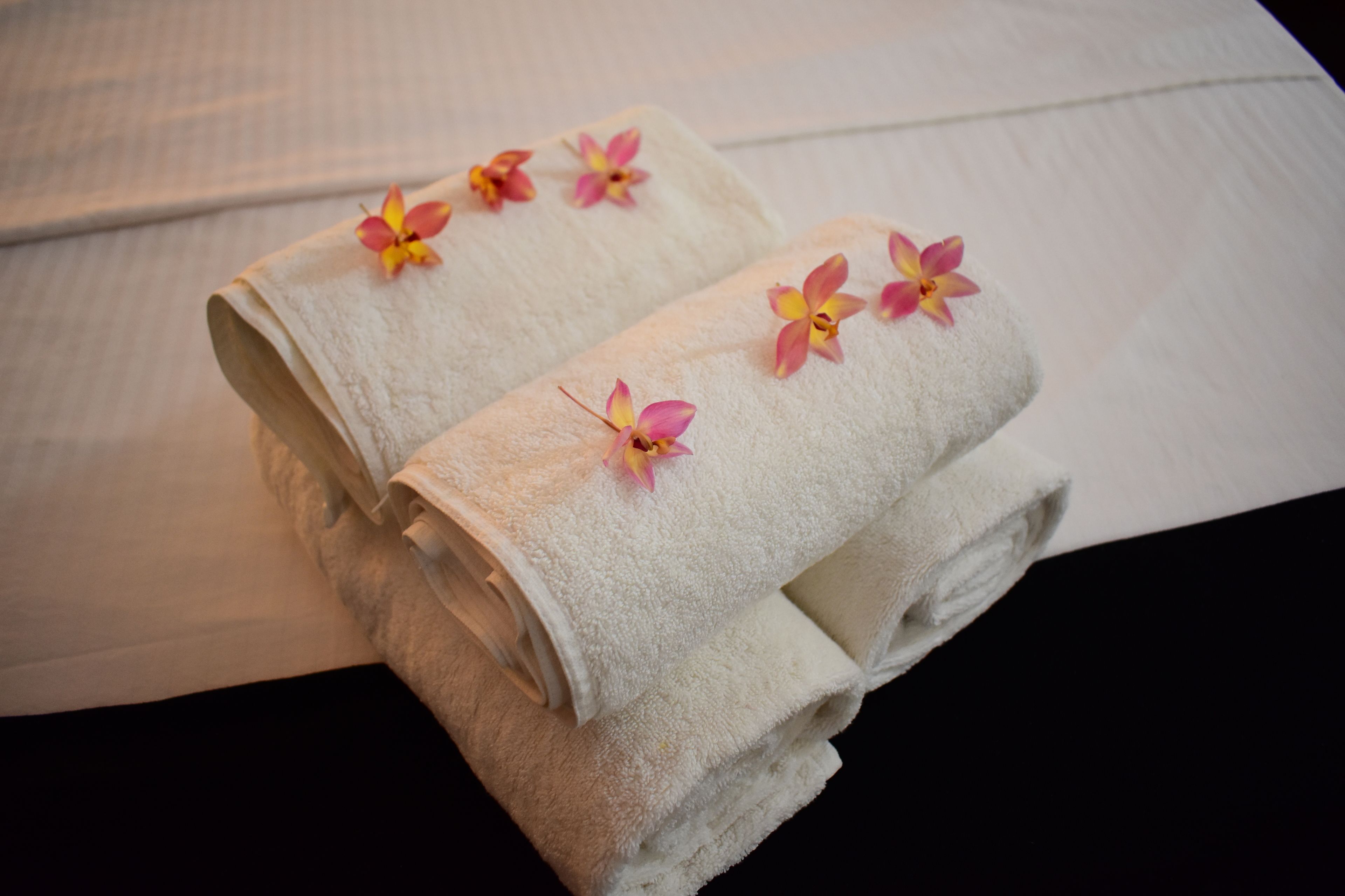 Neatly folded white towels with pink and yellow flowers on a bed.