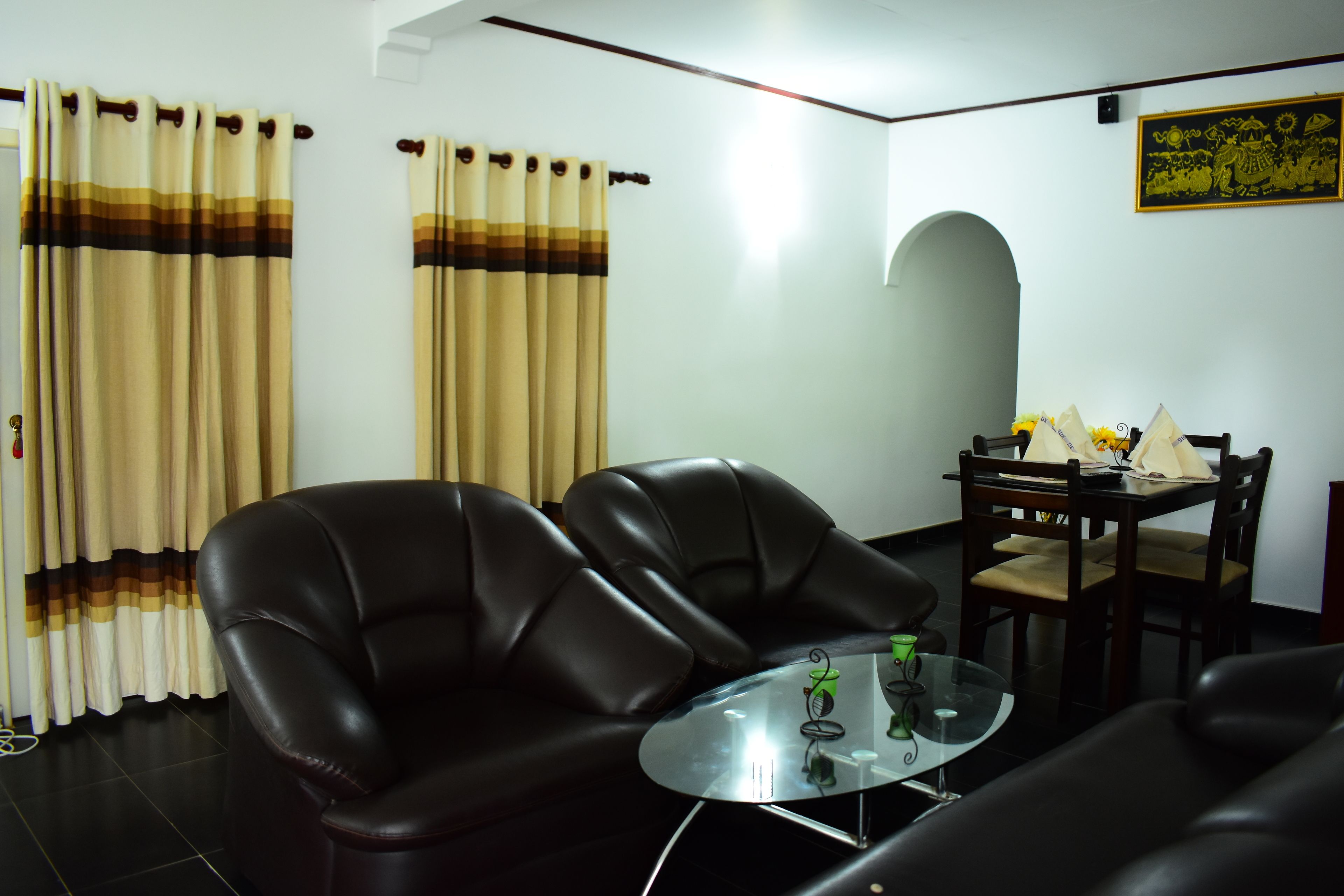 Un salon avec deux canapés en cuir noir, une table basse en verre, une table à manger avec des chaises et des rideaux à motifs rayés.