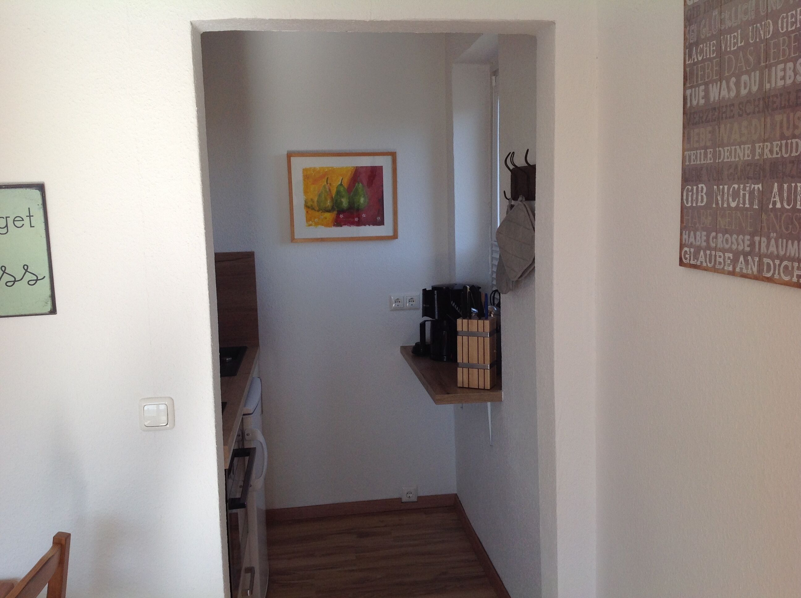 Ein schmaler Flur mit einem Bild an der Wand, einem Regal mit Küchenutensilien und einem kleinen Tisch.