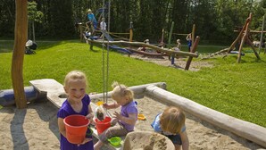 Un parque infantil con zona de juegos de arena, columpios y estructuras para escalar.