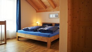 Una cama de madera con colchón azul en una habitación con vigas de madera en el techo y una puerta de madera.