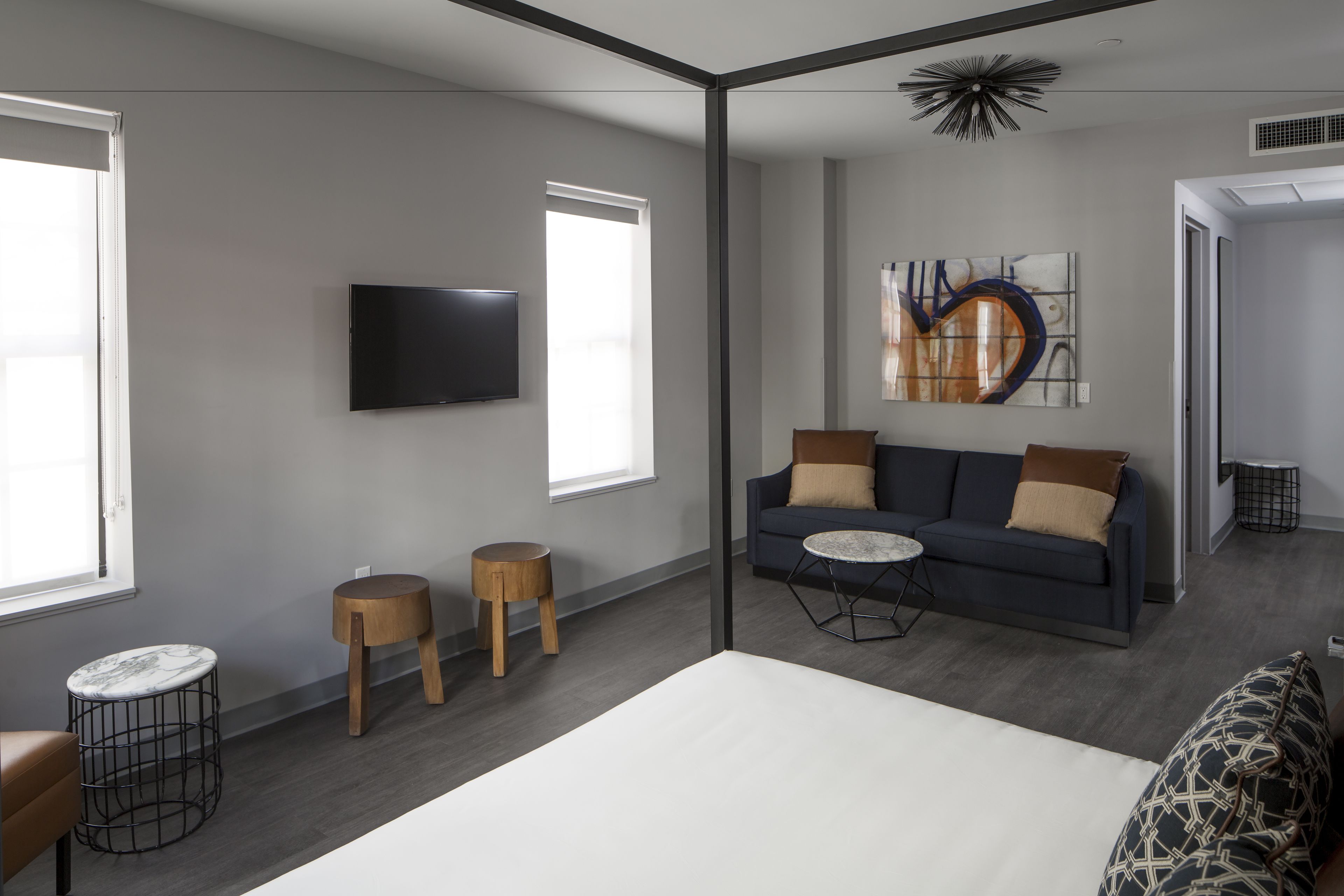 A modern hotel room with a bed, a sofa, a TV, and a large abstract painting on the wall.
