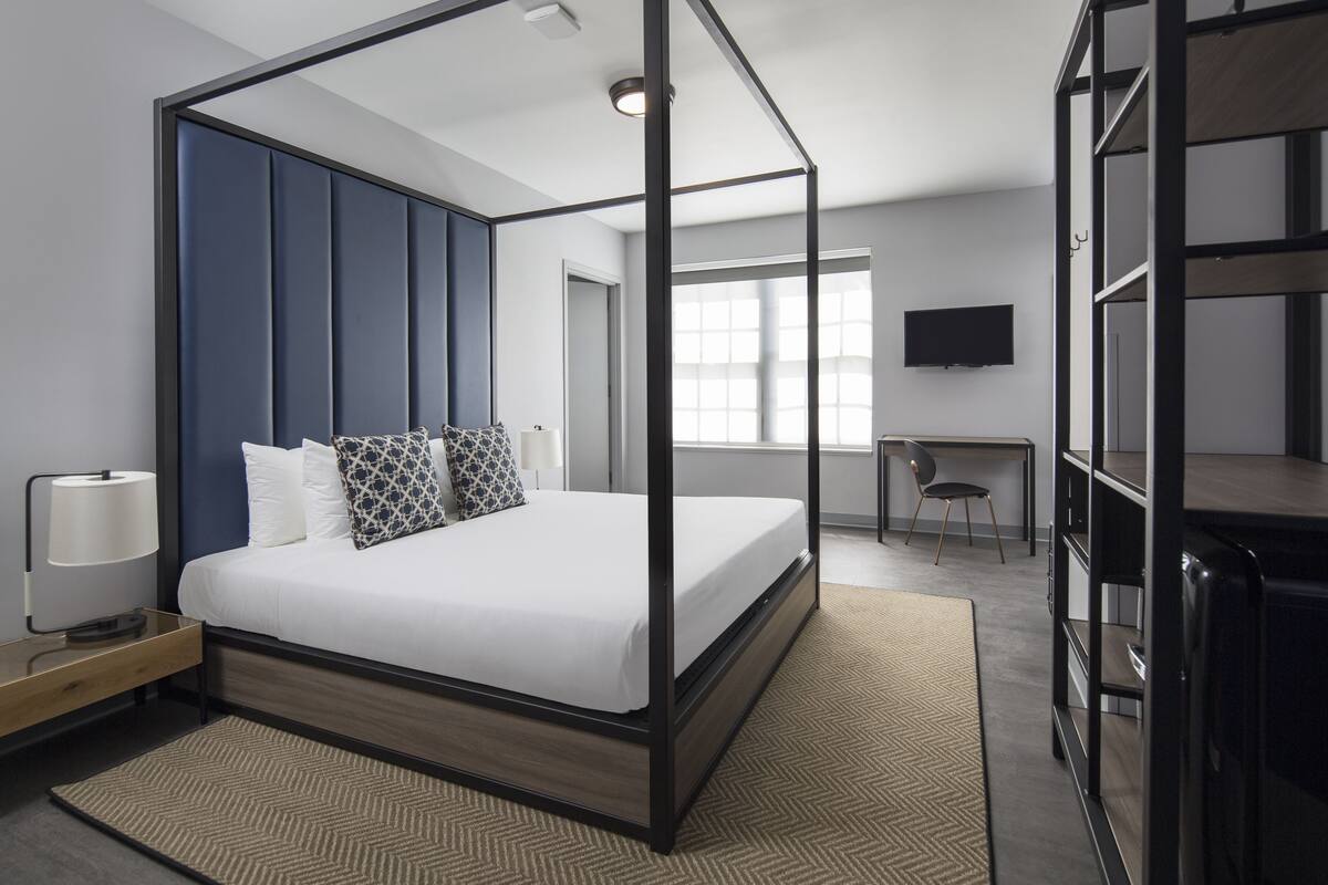 Habitació d'hotel moderna amb un llit amb cortines i un espai de treball, i televisió.
