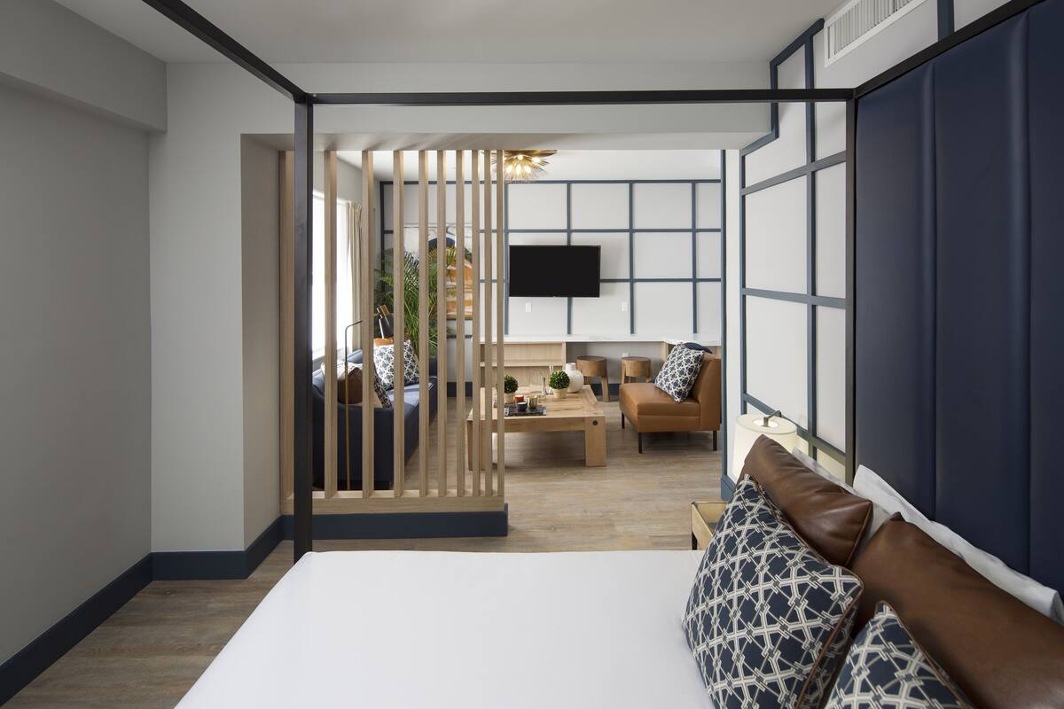 Habitació d'hotel moderna amb un llit gran, una separació de fusta, un sofà, una taula de cafè i una televisió penjada a la paret.