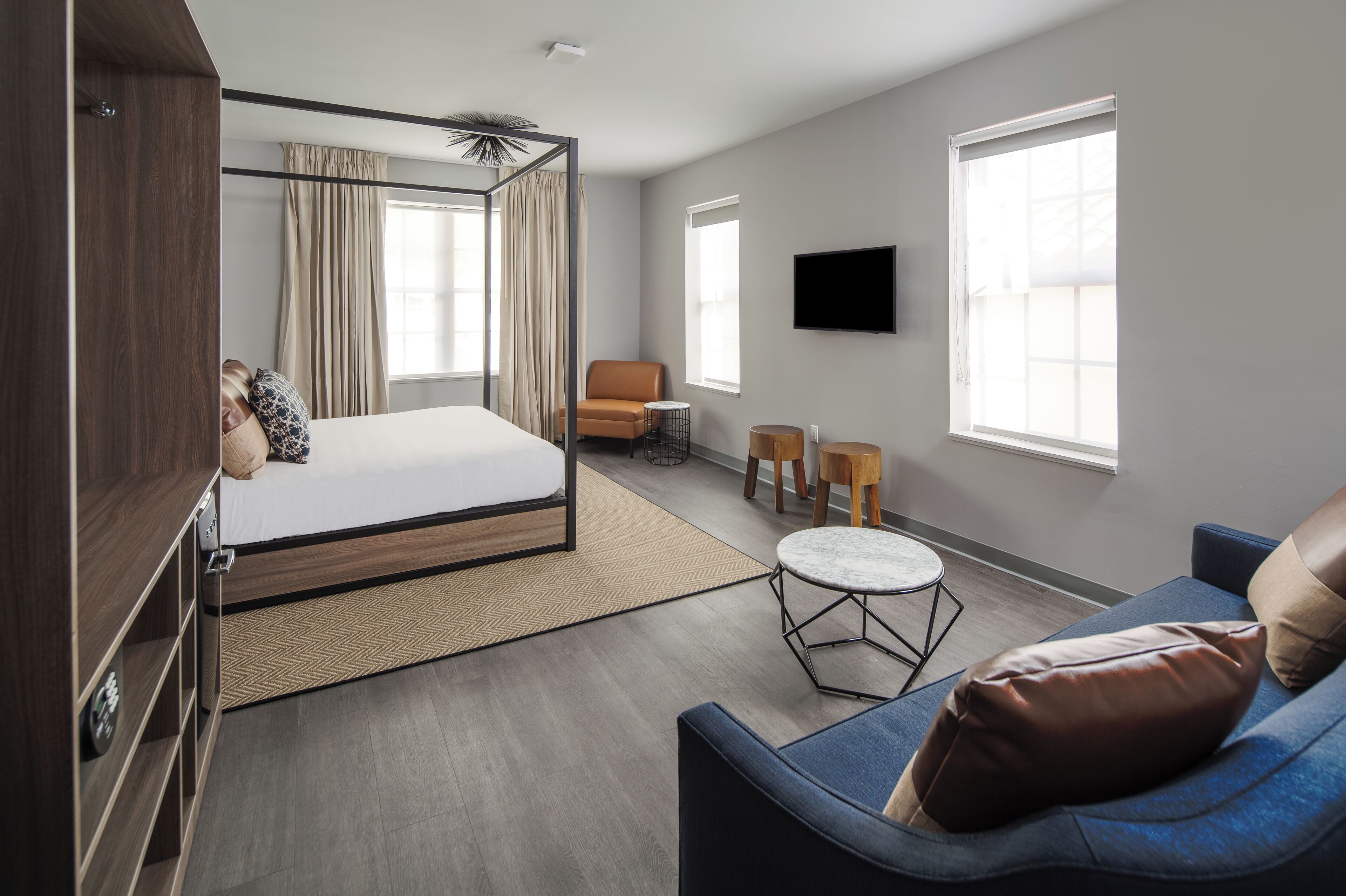 Quarto de hotel moderno com cama de dossel, sofá, mesa redonda pequena e televisão.