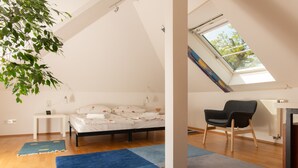 Ein Schlafzimmer mit Bett, Schreibtisch, Stuhl, Dachfenster und einem großen Fenster.