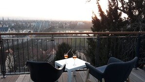 Ein Balkon mit Tisch und zwei Stühlen, mit Blick auf eine Stadtlandschaft inklusive Brücke und Gebäuden.
