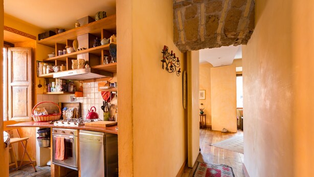 A kitchen with wooden shelves, a stove, and a red kettle. - Charming Bright Colosseum (Roma)