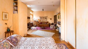 A spacious living area with a large bed, a sofa, and a dining table. There is a bookshelf filled with books and a tapestry on the wall. - Charming Bright Colosseum (Roma)