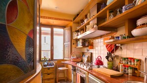 A kitchen with wooden shelves, a stove, a sink, and a window with a view. - Charming Bright Colosseum (Roma)